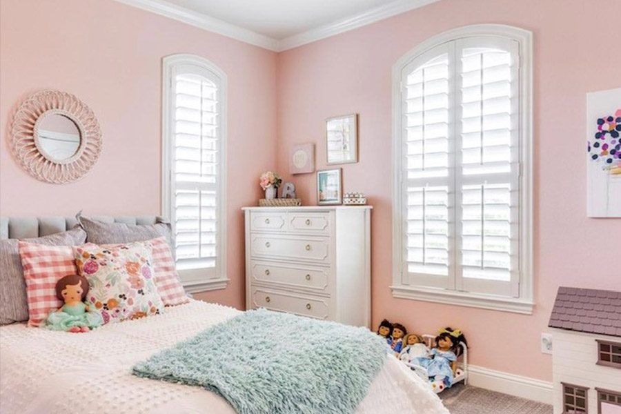 White Polywood shutters on arched windows in a pink child's bedroom.
